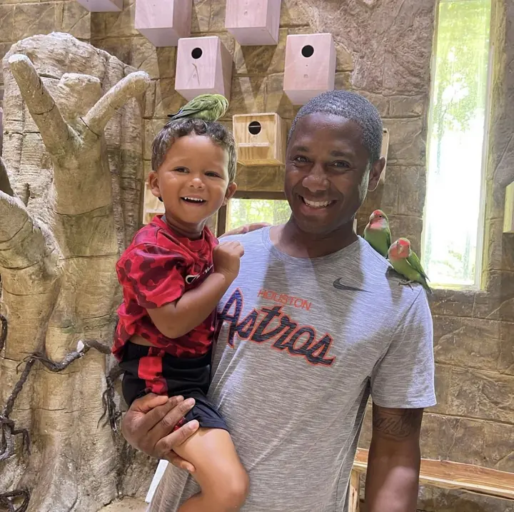 A laughing toddler held by his dad, with a small green bird perched nearby.